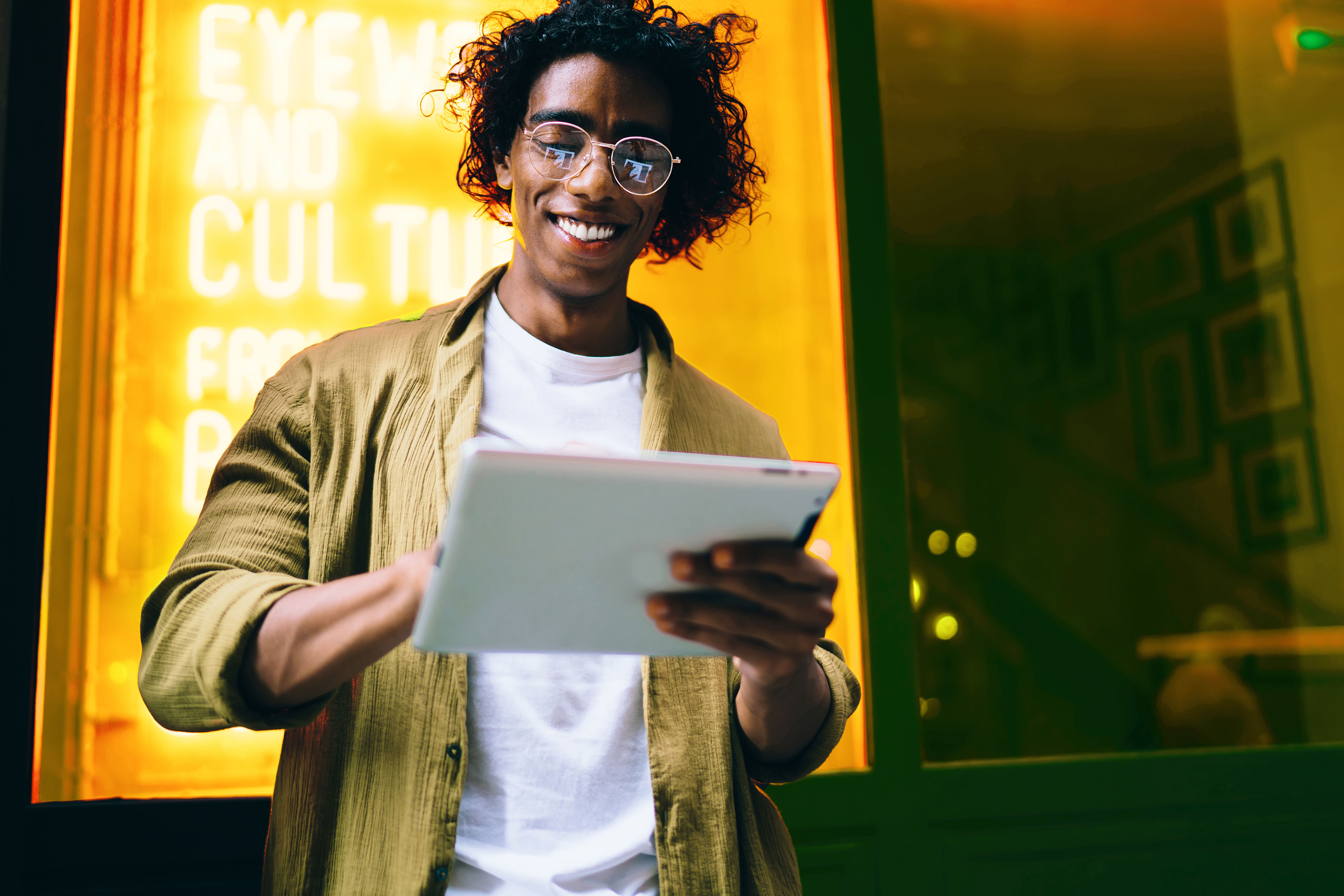 Man reading on tablet outside in front of neon sign