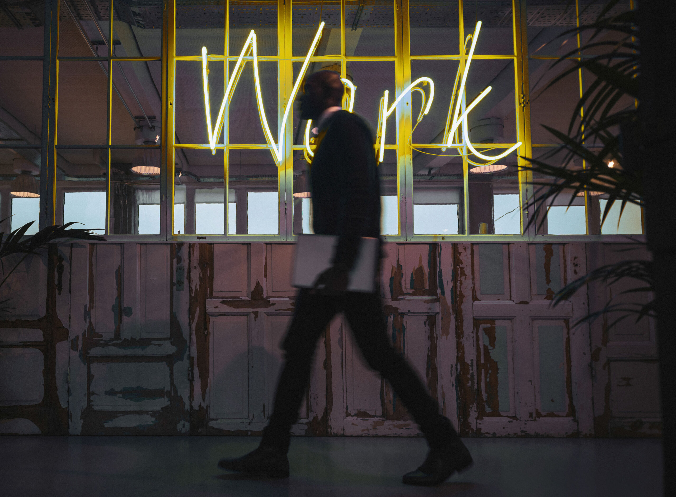 Corridor of a modern office with executive passing by Man at work holding computer walking by neon light